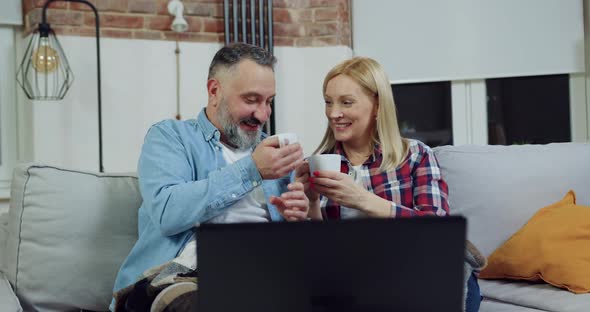 Couple Sitting at Home in the Evening and Clinking Tea Cups During Watching Exciting Movie