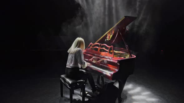 The Pianist Plays on the Stage in the Rays of Spotlights