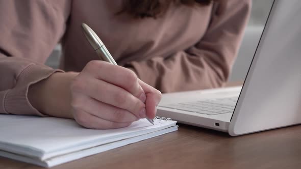 A Girl Takes Notes in a Notebook From Her Laptop