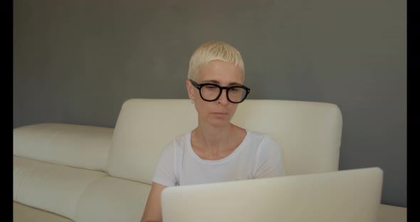 Blond woman with blue eyes on sofa with laptop