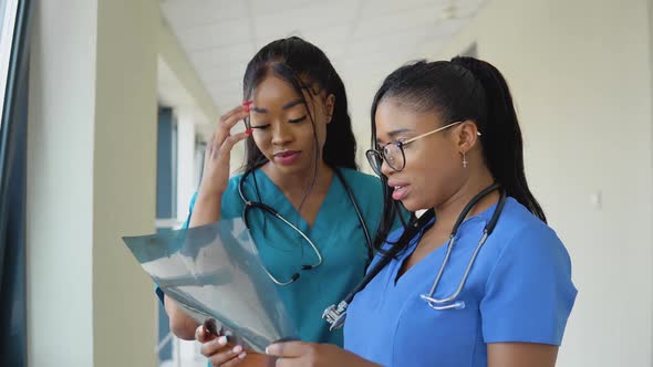 Two Young AfricanAmerican Female Doctors in Sinfh Suits Examine an Xray and Discuss It