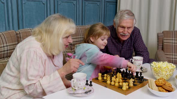 Mature Grandmother Grandfather with Child Girl Grandchild Playing Chess Game with on Table in Room