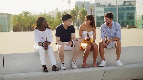 Four Young Happy Cheerful Friends of Different Races Talking and Enjoying Alcoholic Drinks at Sunset