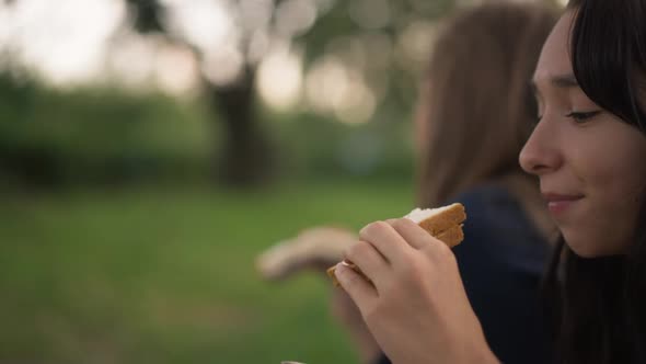 Side View Teenage Girl on the Right Eating Sandwich with Blurred Friend at Background