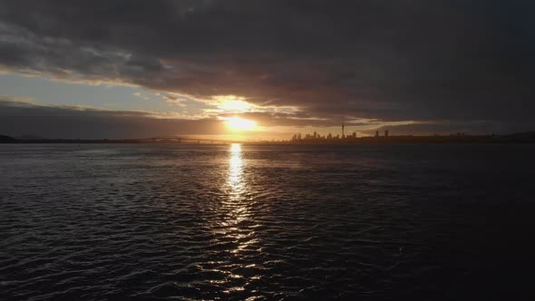 AERIAL flying low and rising over Auckland Harbour with golden sunrise cityscape