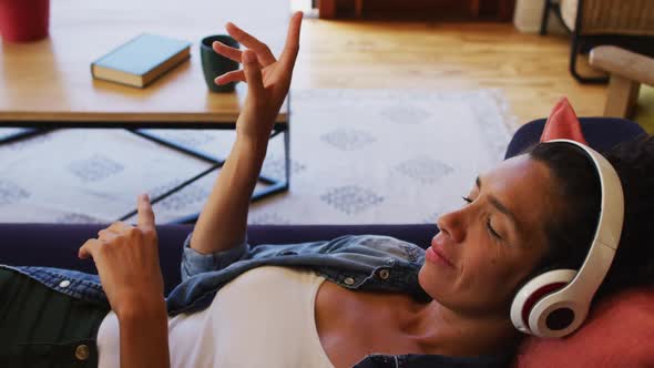 Caucasian woman listening to music with headphones on, lying on sofa at home