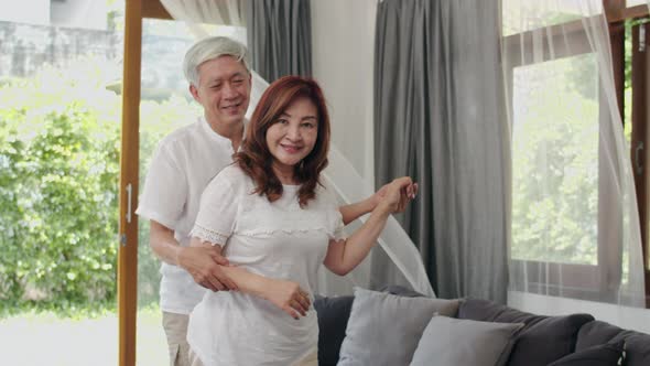 Asian elderly couple dancing together while listen to music in living room at home