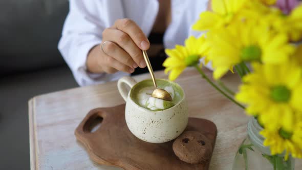 Hand Stirring Matcha Tea Latte the Spoon and Shows the Foam to the Camera