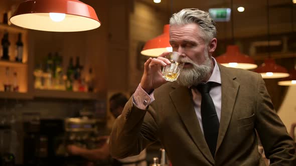 solid gray-haired man drinking his whiskey in a night bar