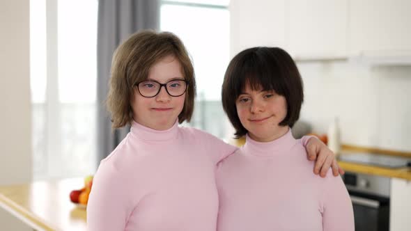 Portrait of Two Cute Girls with Down Syndrome Standing Together Embracing at Home