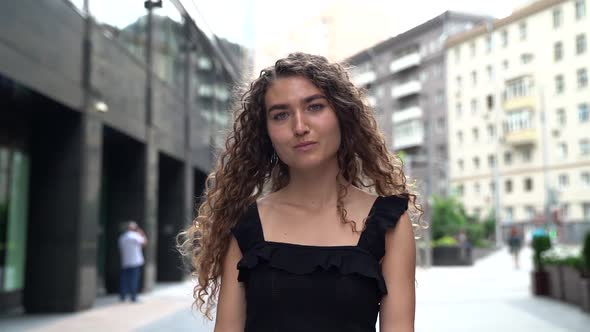 Close-up Portrait of a Young Curly-haired Woman , She Is on a City Street in the Afternoon, Walking