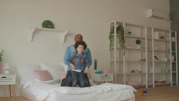 Joyful Black Father and Little Son Jumping on Bed