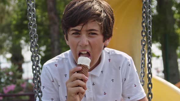 Teenager Boy Swinging On Swing In Park And Eating Ice Cream