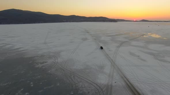 Drone View of a Small Truck Driving Across the Frozen Sea at Sunset