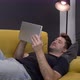 Young Unshaven Handsome Smiling Guy Messaging Online Lying on Sofa with Tablet - VideoHive Item for Sale