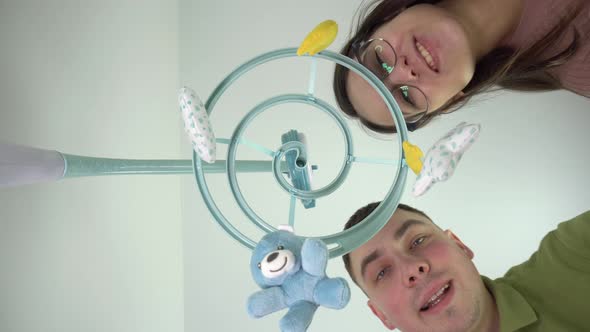 Young Parents Look at a Newborn Baby Lying in a Cradle with a Baby Mobile with Toys