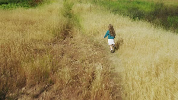 Happy Little Girl Running By Scenic Meadow with High Green Grass on Summer Day