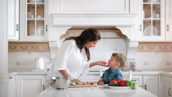 Smiling Caring Woman Feeding Little Cute Boy By Fresh Organic Vegetables While Cooking