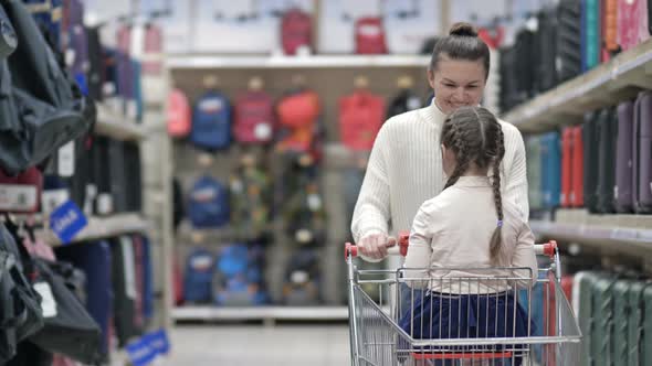 Young Woman Rolls a Shopping Cart in Which Her Little Daughter Is Sitting