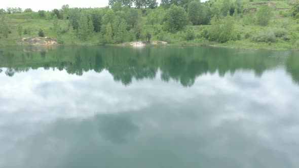 Reflections of sky and trees on pond surface 4K aerial footage