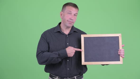 Happy Macho Mature Businessman Holding Blackboard and Giving Thumbs Up