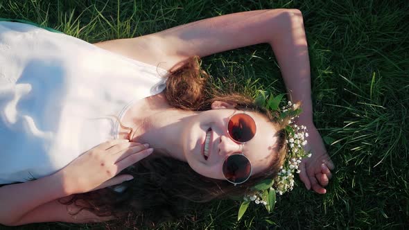 SLOW MOTION: Top view shot of a Caucasian girl in a white floral dress lying in grass