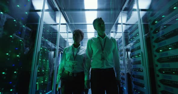 Workers in a Data Center Walking Between Rows of Server Racks