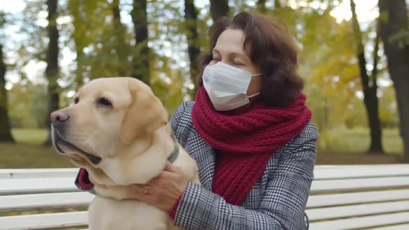 Portrait of Aged Woman Wearing Safety Mask Hugging Dog Sitting on Park Bench
