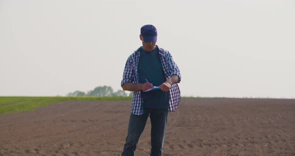 Mature Male Farmer Writing On Clipboard At Farm. Modern Agriculture