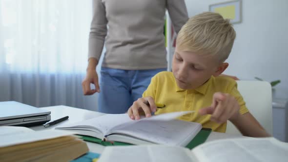 Loving Mother Kissing Head of Little Diligent Son Doing Homework, Education