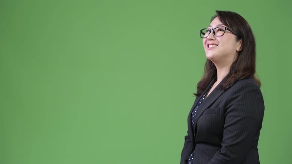 Profile View of Mature Happy Asian Businesswoman Against Green Background