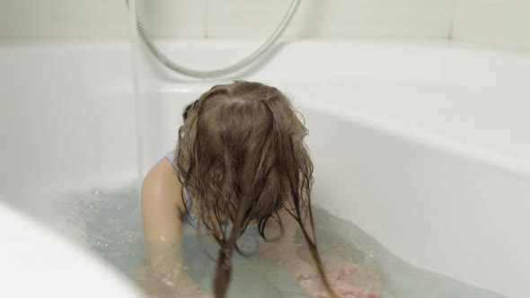 Cute Blonde Girl Takes a Bath in Swimwear. Little Child Washes Her Head