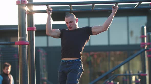 Young Sportive Man Training His Hands on the Bars Outdoors