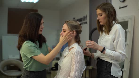 Make-up artist preparing to apply makeup to woman sitting in front of mirror.