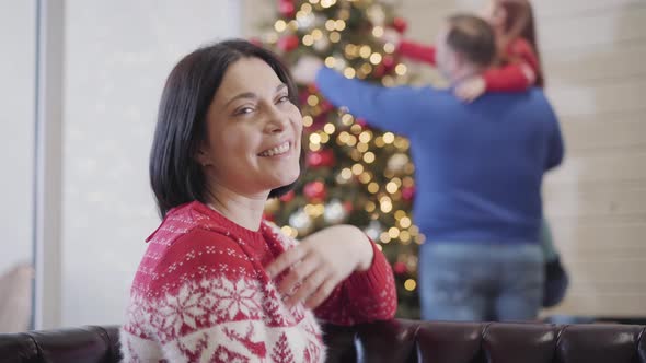 Portrait of Happy Woman Smiling at Camera and Looking Back at Blurred Husband and Daughter