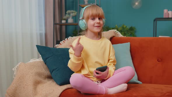 Child Girl Kid with Smartphone in Headphones Dancing Singing Listening Music at Home Alone on Sofa