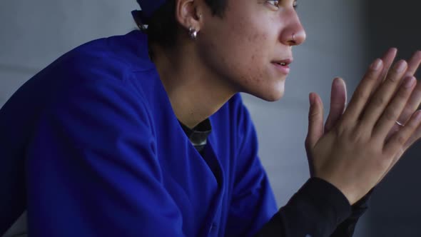 Nervous mixed race female baseball player, sitting on bench waiting, rubbing hands