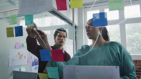 Man and woman discussing over memo notes on glass board at office