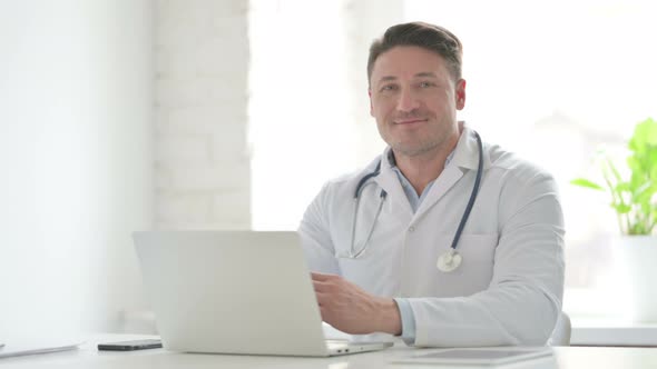 Male Doctor Smiling at Camera while using Laptop in Office