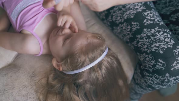 Mommy Gives Eye Drops to Little Girl Lying on Soft Bed