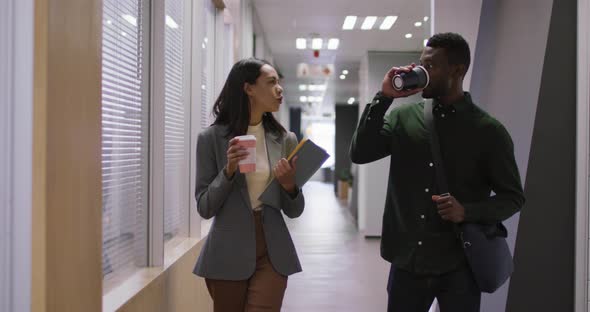 Two happy diverse business people working together, talking, drinking coffee in modern office