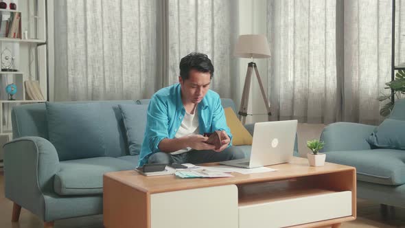 Asian Man Looking At The Bill On Hand And Checking Money On The Wallet Before Shaking His Head