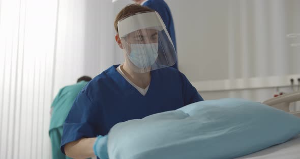 Male Nurse in Safety Gloves and Mask Working at Hospital Making Bed and Changing Sheets