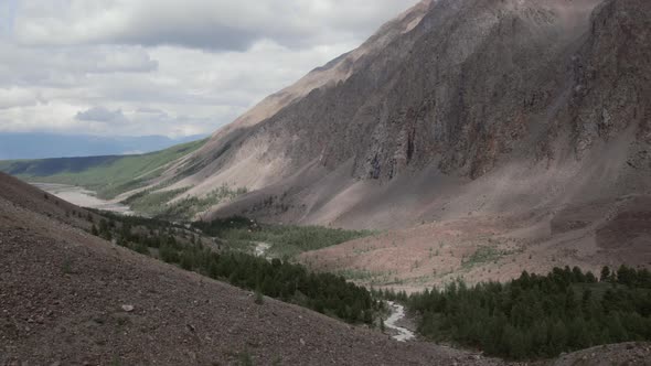 Mountains of Aktru valley with river and forest under white clouds in Altai