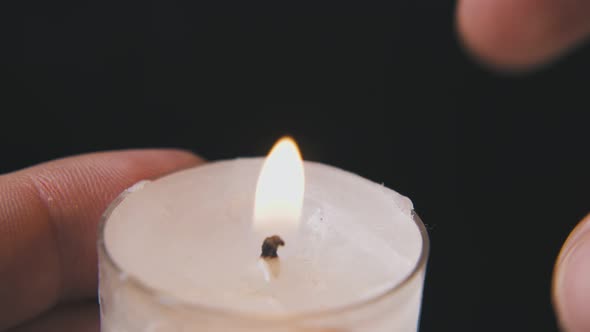 Man Lights Candle in Plastic Holder on Dark Background