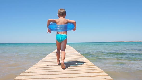 Little Boy in Swimming Shorts Runs Along a Wooden Pier To the Azure Sea on a Sunny Clear Day, Slow