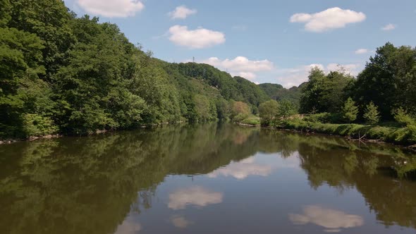 Low drone flight over a wide brown river that reflects the beautiful sky above.