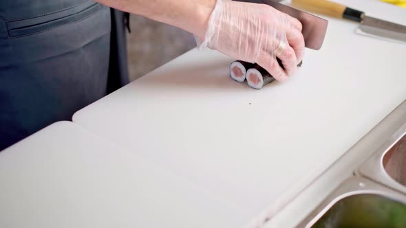 Male Chef Hands Cutting Prepared Maki Sushi Roll on Board in Restaurant Kitchen