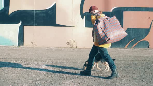 A Homeless Man is Walking Along the Street with His Dog