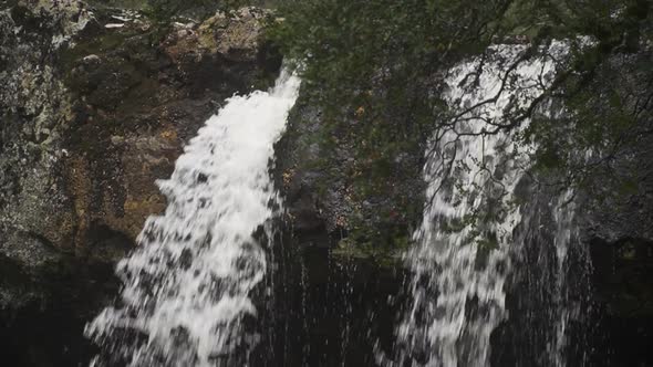 A slow motion waterfall in a rain forest in front of a cave, close up